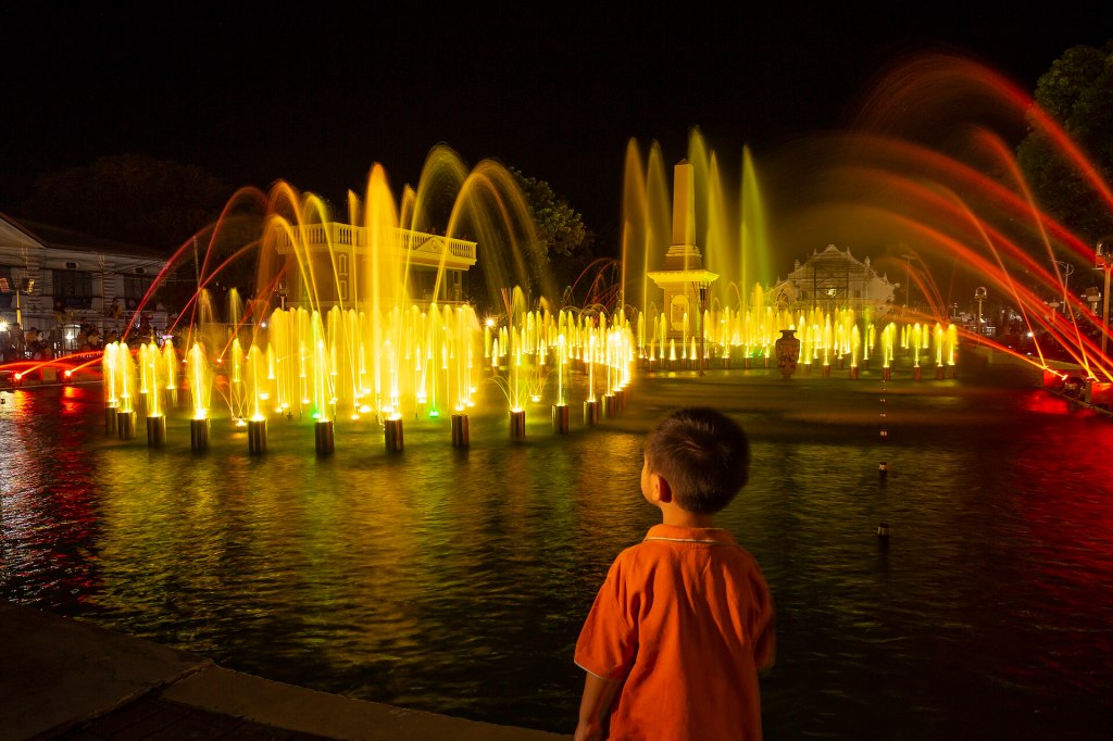 Colorful dancing fountain at Plaza Salcedo in Vigan at night, with a child watching in the foreground