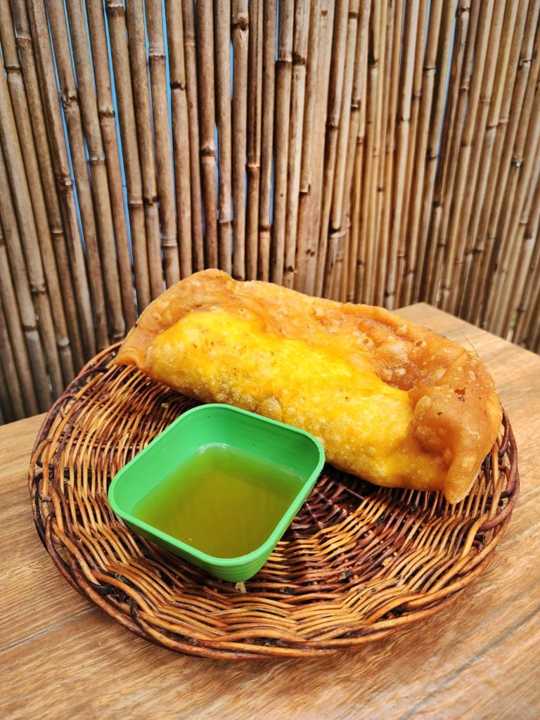 A crisp orange Vigan empanada served in a woven basket with a small dish of vinegar
